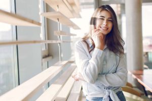 smiling girl in a blue shirt standing near window AW6AENP