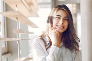 smiling girl in a blue shirt standing near window AW6AENP11