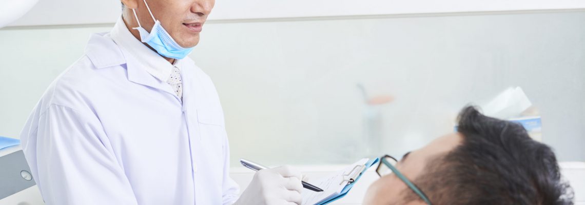 Horizontal shot of male dentist consulting young man in dentist's office