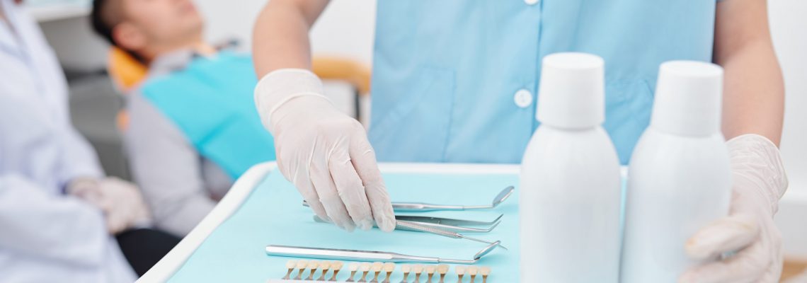 Cropped of assistant preparing tray for dentist and putting tools, teeth color palette and bottles of antiseptic mouthwash product